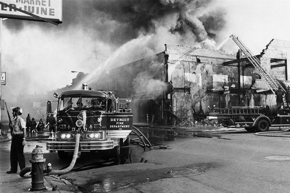 A policeman stands guard in a Detroit street on July 25, 1967 as firefighters try to extinguish a burning building during riots that erupted in Detroit following a police operation.        (Photo credit should read -/AFP/Getty Images)